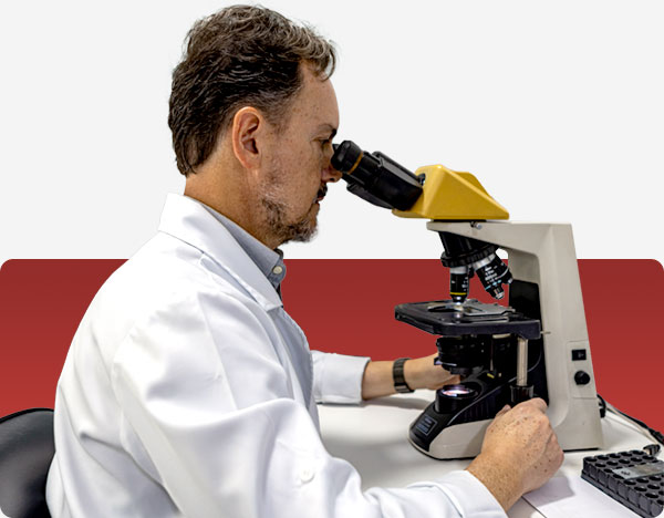 Foto do Dr. Moacir sentado em uma cadeira manipulando um microscópio